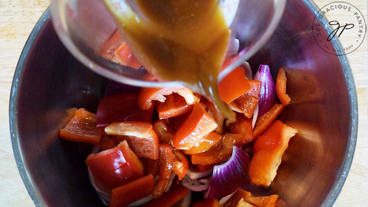 A large mixing bowl filled with peppers and onions getting teriyaki marinade poured over them.