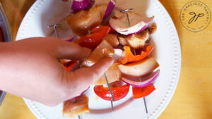 Layering the chicken and vegetables on metal skewers over a white plate.