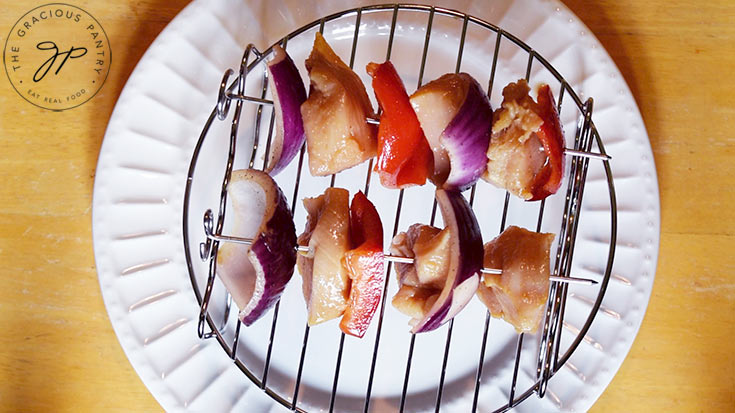 An air fryer skewer rack sits on a white plate. Two kabobs lay on the rack, ready to go into the air fryer.