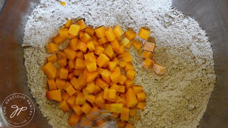 The cut butternut squash pieces being stirred into the dry mix.