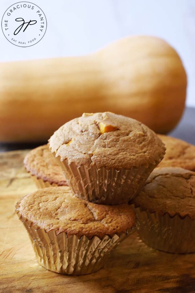 A stack of muffins on a cutting board with a whole butternut squash laying behind them.