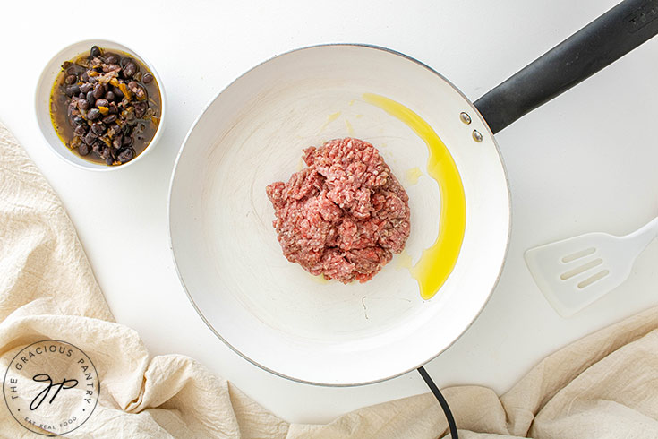 Raw ground meat in a white skillet.