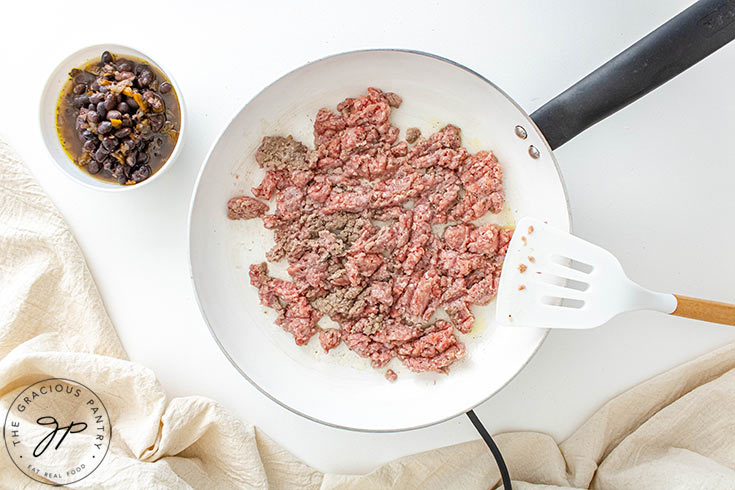 Scrambling ground meat with a spatula in a white skillet.