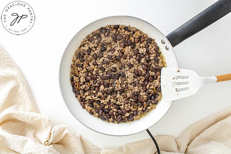 Beans added to ground meat in a white skillet.