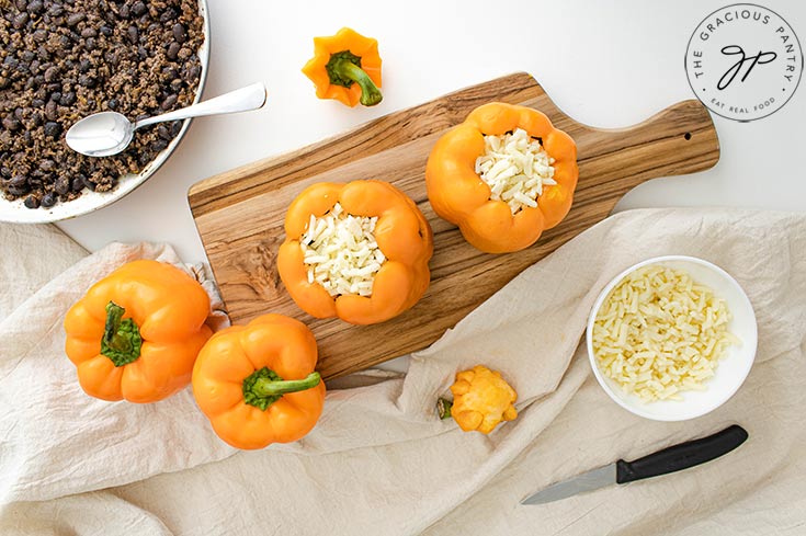 Topping Jack-O-Lantern Stuffed Peppers with cheese.