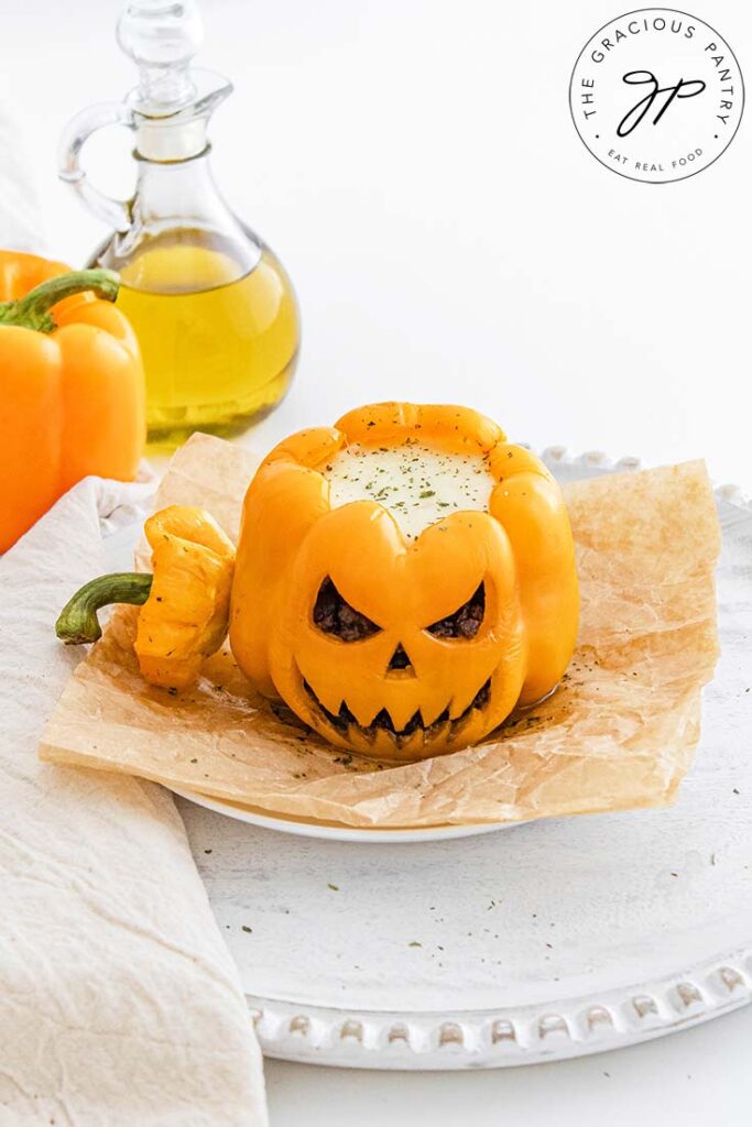 A slightly overhead view of a Jack-O-Lantern Stuffed Pepper on a white platter. A second pepper sits behind it on the table.