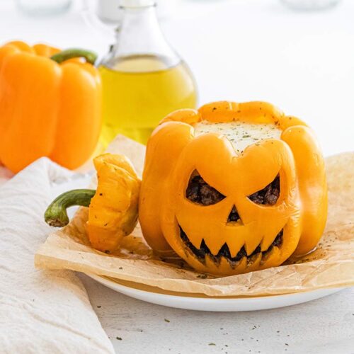 A Jack-O-Lantern Stuffed Pepper sits on a white plate with it's top resting to the side.