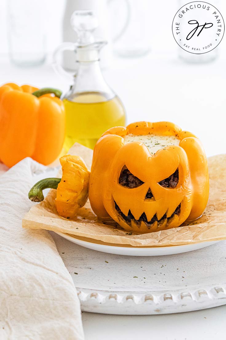 A Jack-O-Lantern Stuffed Pepper sits on a white plate with it's top resting to the side.