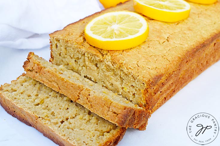 The finished loaf of Lemon Bread on a white background with two slices sliced off and laying at the front of the loaf.