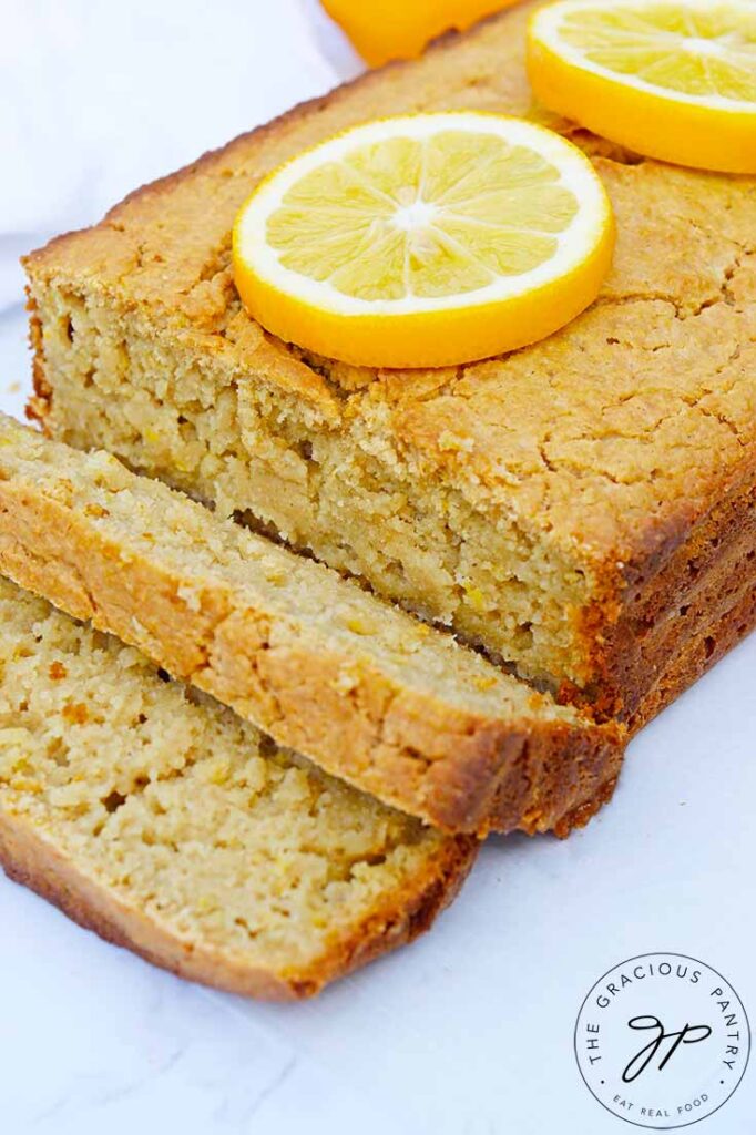 The loaf of Lemon Bread on a white background. Two slices are sliced at the front of the loaf.