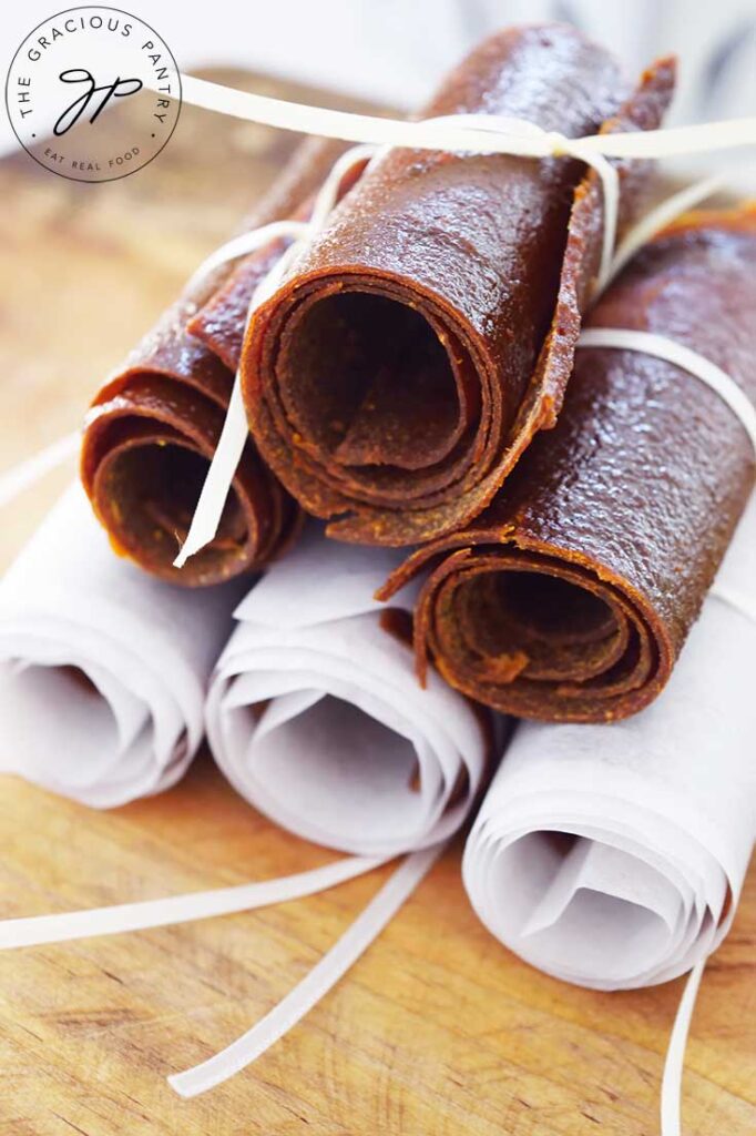 A side view of a stack of Pumpkin Fruit Leather roll-ups on a cutting board.