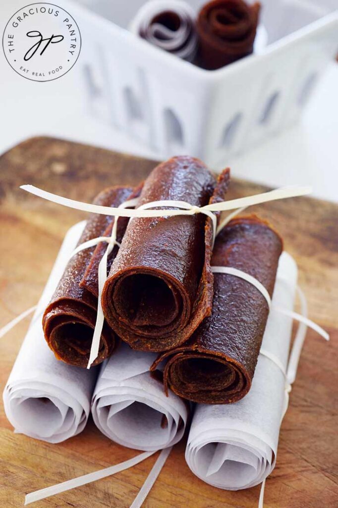 A pile of Pumpkin Fruit Leather sits on a cutting board with a couple more in a white basket behind it.