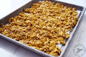 The raw granola spread out over a parchment-lined baking pan.
