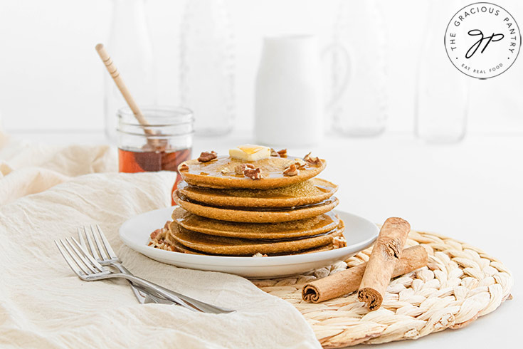 The finished Pumpkin Oatmeal Pancakes on a white plate, topped with a pat of butter, chopped pecans and some honey.