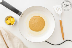 A single Pumpkin Oatmeal Pancake cooking in a white skillet.