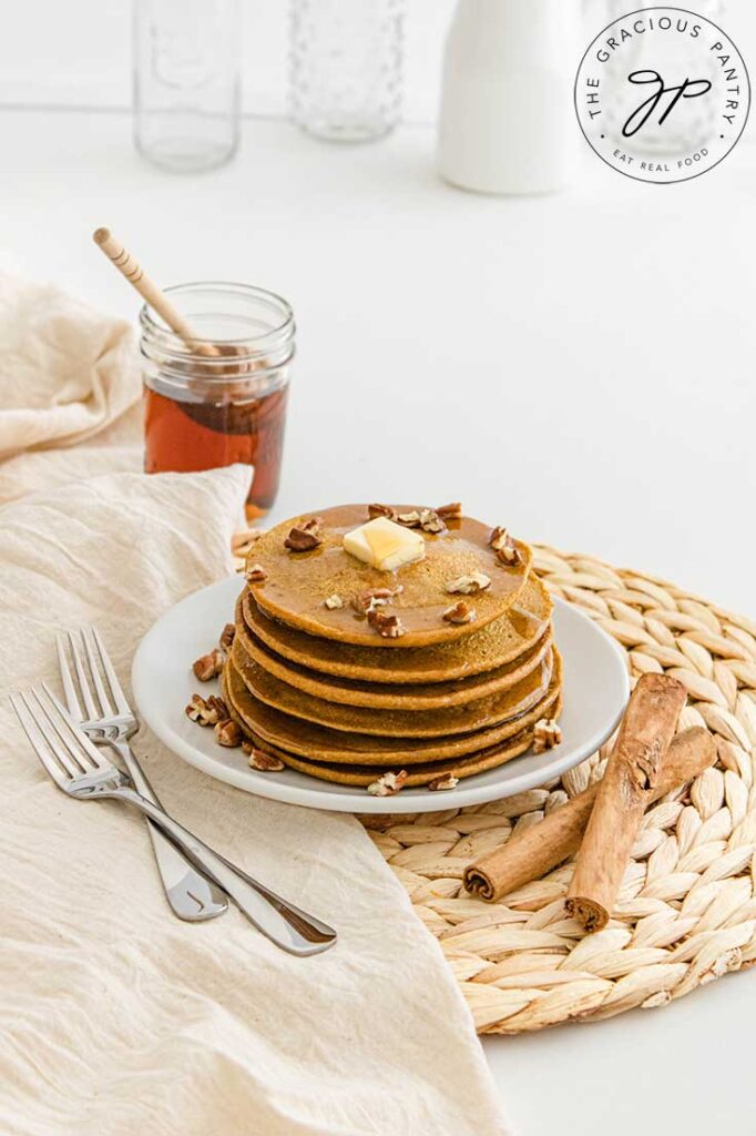 A white plate holds a stack of Pumpkin Oatmeal Pancakes with two forks resting to the left side of the plate.