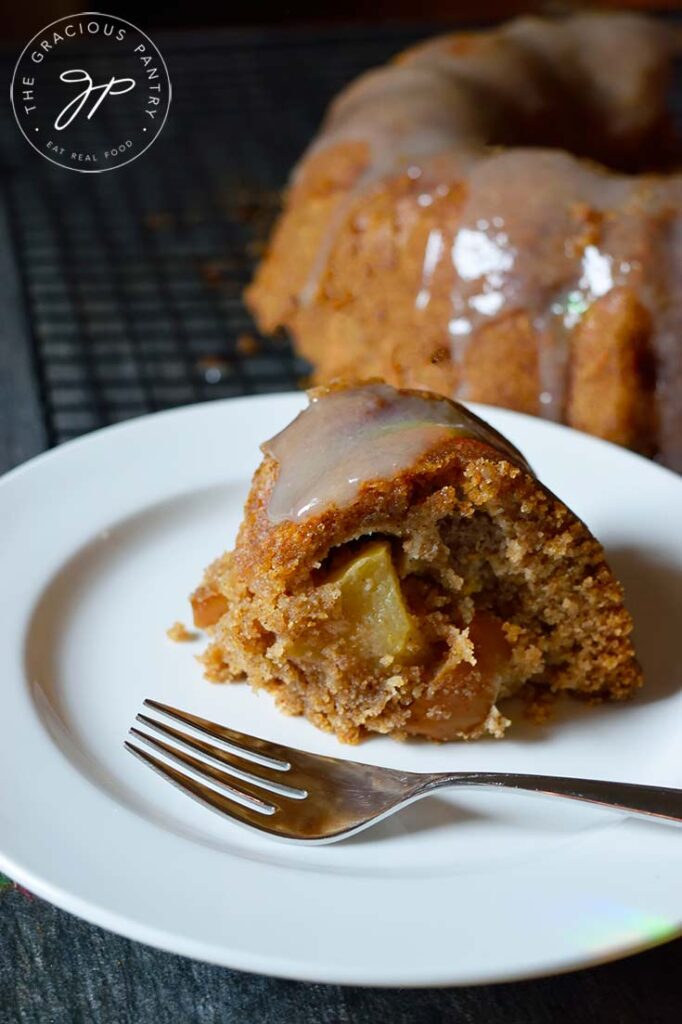 A slice of Spiced Apple Bundt Cake sits on a white plate. A fork rests to the side of the slice.