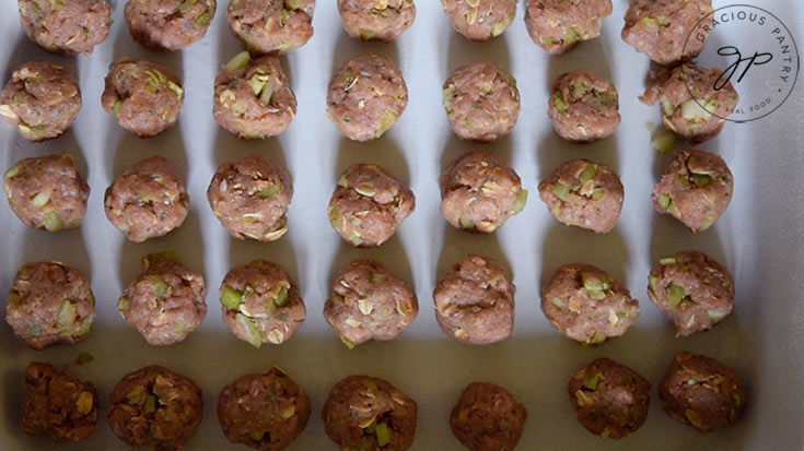 The rolled meatballs lined up in a baking pan.