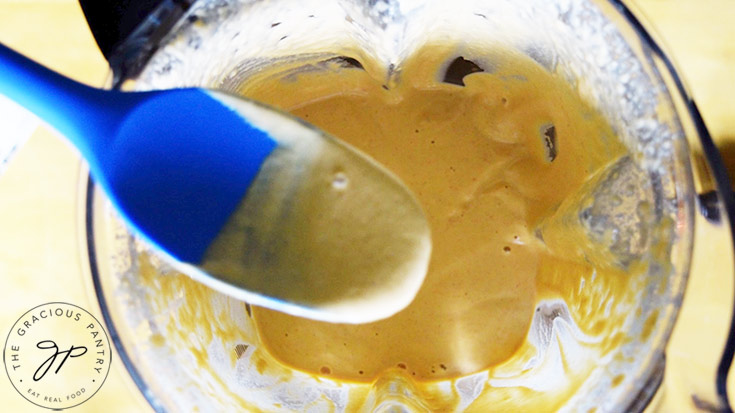 A blue spatula lifts some of the blended sauce out of the blender and towards the camera.
