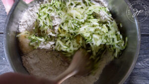 Grated zucchini being mixed into a bowl of flour.