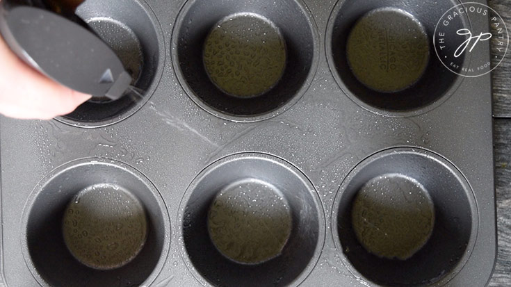 Spraying the muffin pan with an oil sprayer.