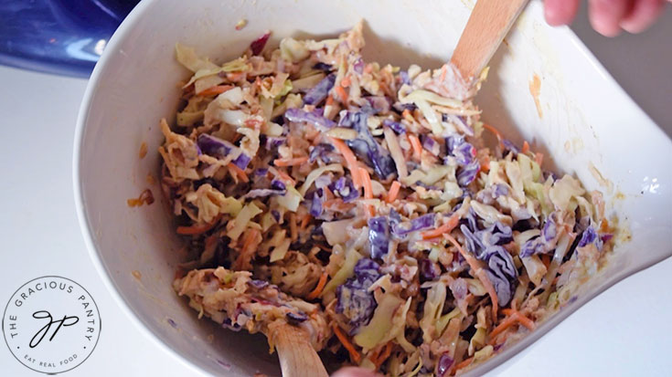 The Apple Slaw being tossed in a large white mixing bowl.