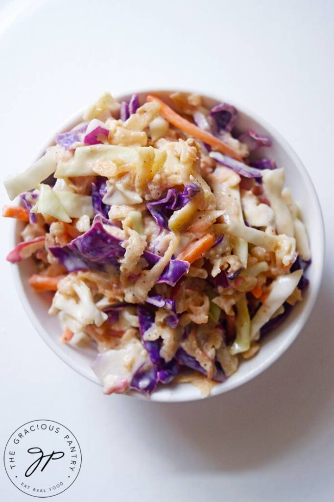An overhead view looking down into a white bowl of apple slaw, sitting on a white table.