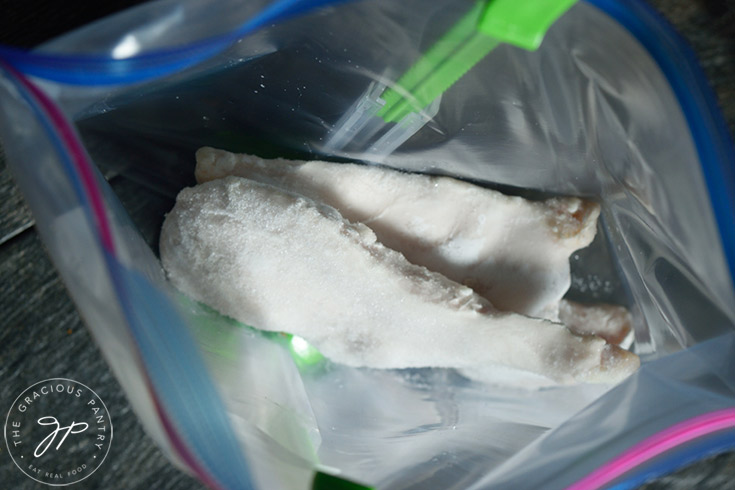 Two frozen chicken breasts added to the freezer bag.