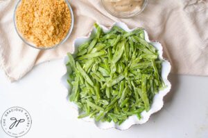 Green beans laid out in a white, round, fluted casserole dish.
