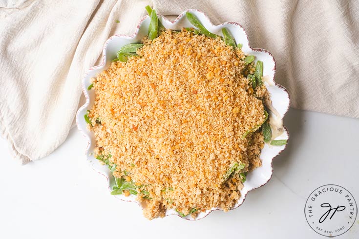 Green beans topped with cream of mushroom soup and bread crumbs, in a round, white casserole dish.