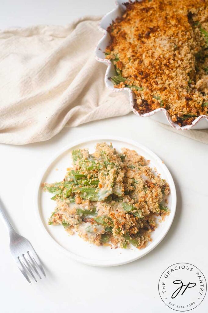 An overhead shot of Healthy Green Bean Casserole on a white plate. The casserole dish sits behind it.