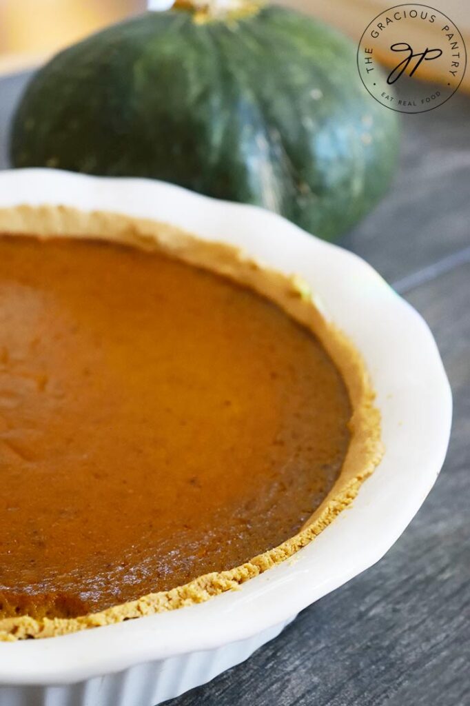 A whole Kabocha pie on a counter top with a whole Kabocha squash sitting behind it.