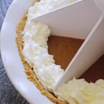 A side view of a whole kabocha pie with a white pie cutter pressed into the pie.