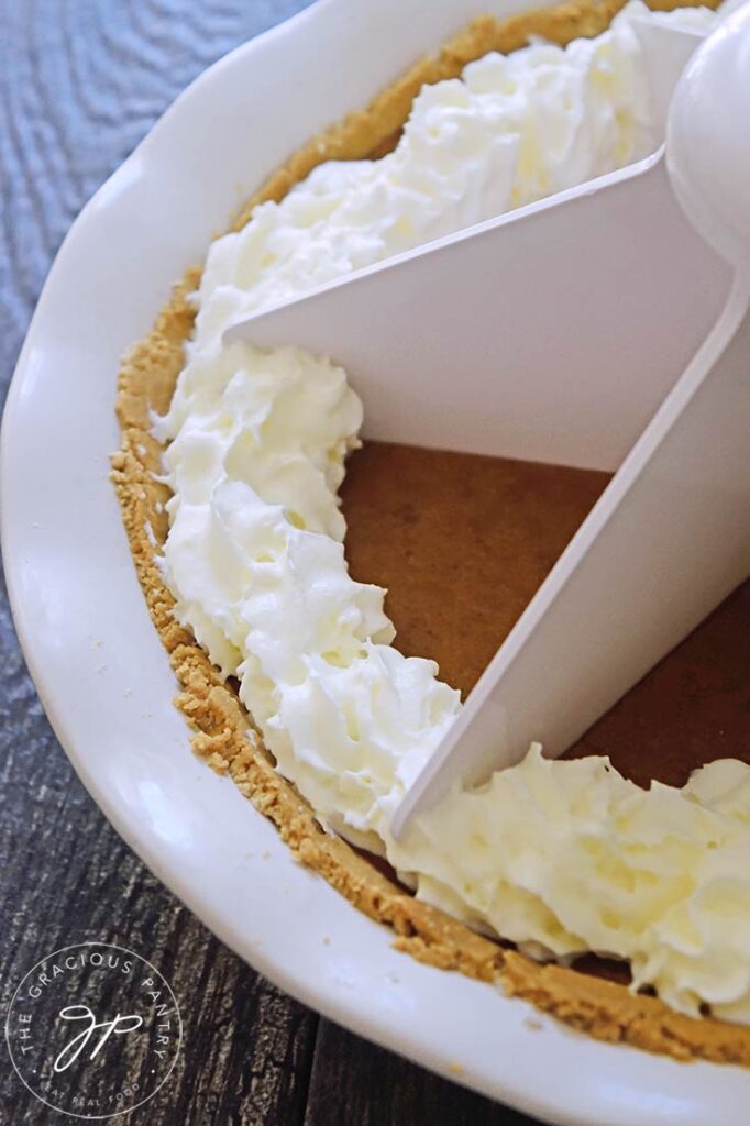 A side view of a whole kabocha pie with a white pie cutter pressed into the pie.