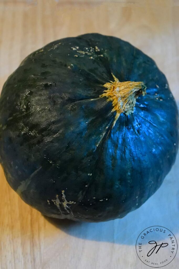 An overhead view of a whole kabocha squash sitting on a cutting board.