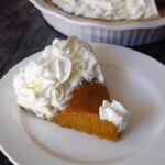 A slice of Kabocha pie with whipped cream on a white plate.