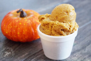The finished Pumpkin Ice Cream recipe in a white bowl. A small pumpkin sits to the left.