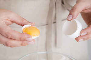 Two hands separate an egg over a glass bowl.