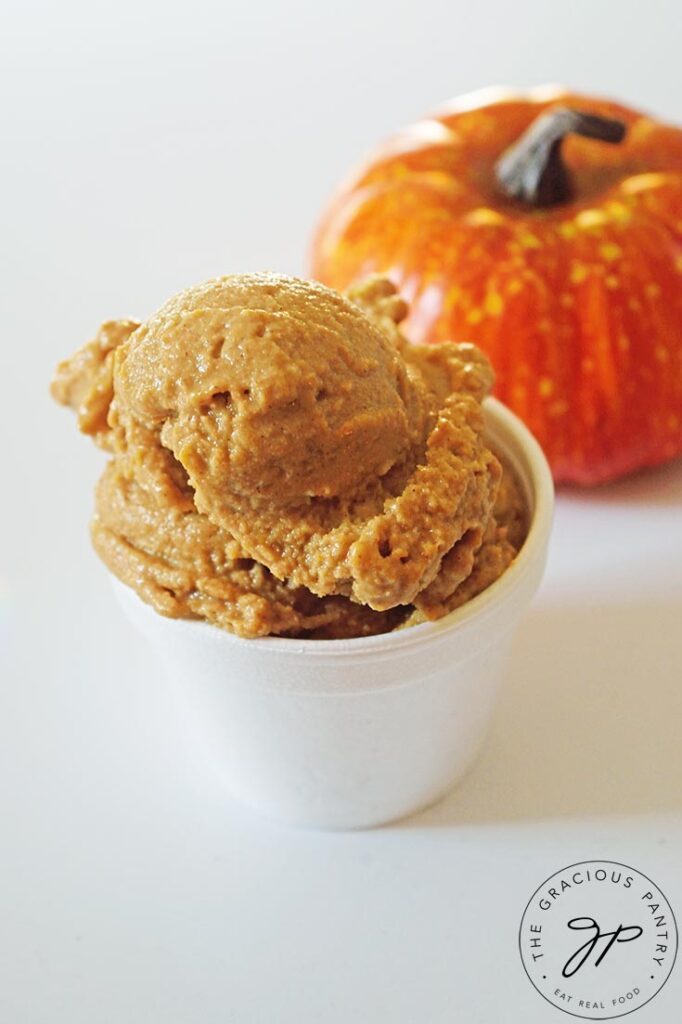 An up close shot of some Pumpkin Ice Cream in a white bowl. A small pumpkin sits behind it to the right.