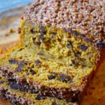 A loaf of Snickerdoodle Pumpkin Bread sits on a cutting board with the first two slices laying at the front of the loaf.