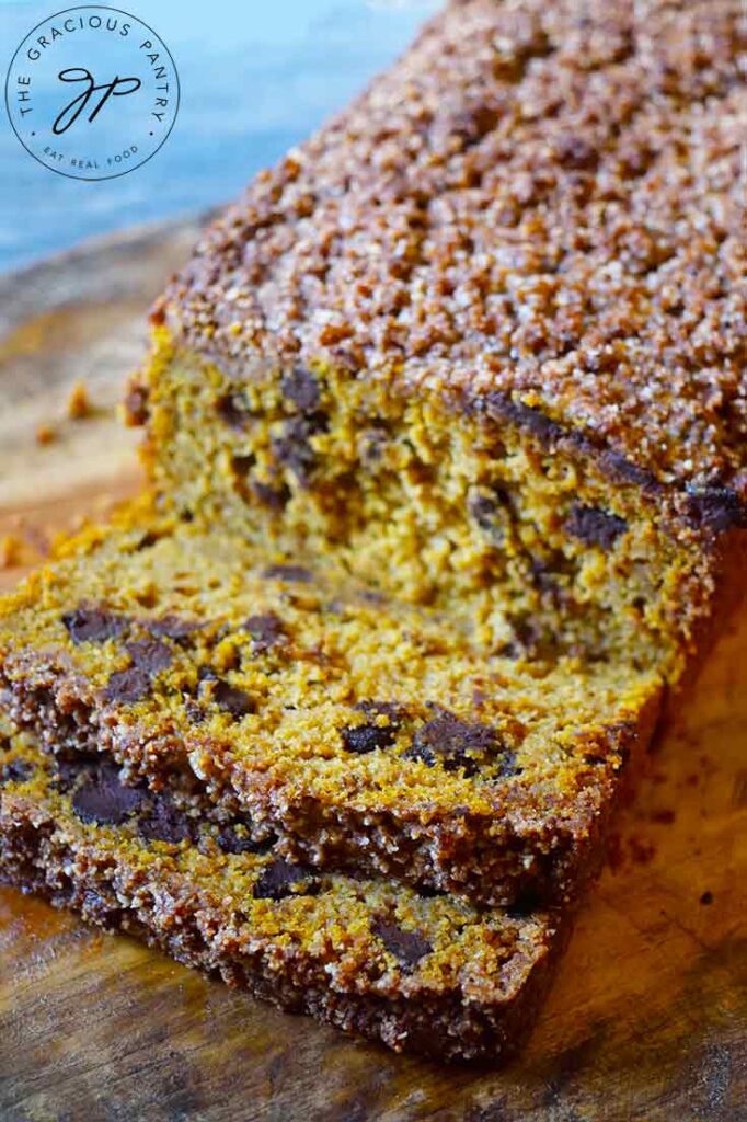 A loaf of Snickerdoodle Pumpkin Bread sits on a cutting board with the first two slices laying at the front of the loaf.