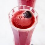 An overhead side view of two glasses filled with Cranberry Mimosa Mocktail. A fresh cranberry floats in each glass.