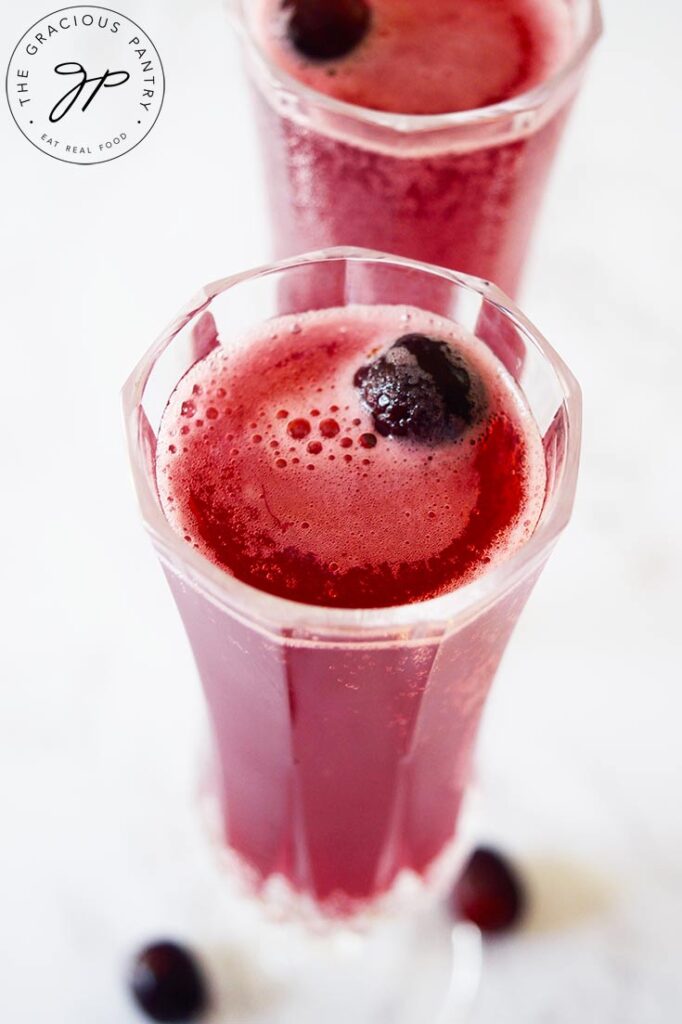An overhead side view of two glasses filled with Cranberry Mimosa Mocktail. A fresh cranberry floats in each glass.