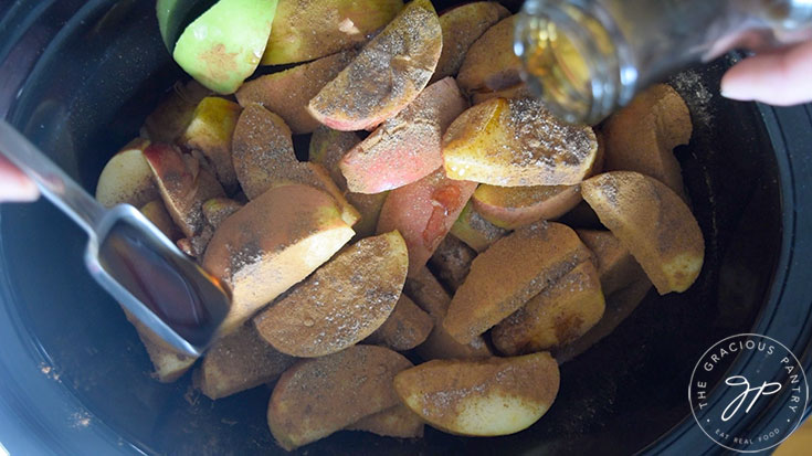 Cut apples in a black crock, covered in spices and maple syrup.