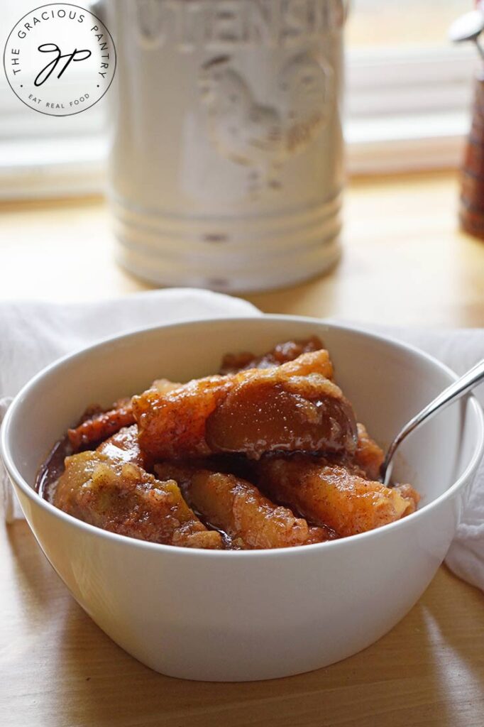 A white bowl of Crockpot Cinnamon Apples sitting on a wooden table.