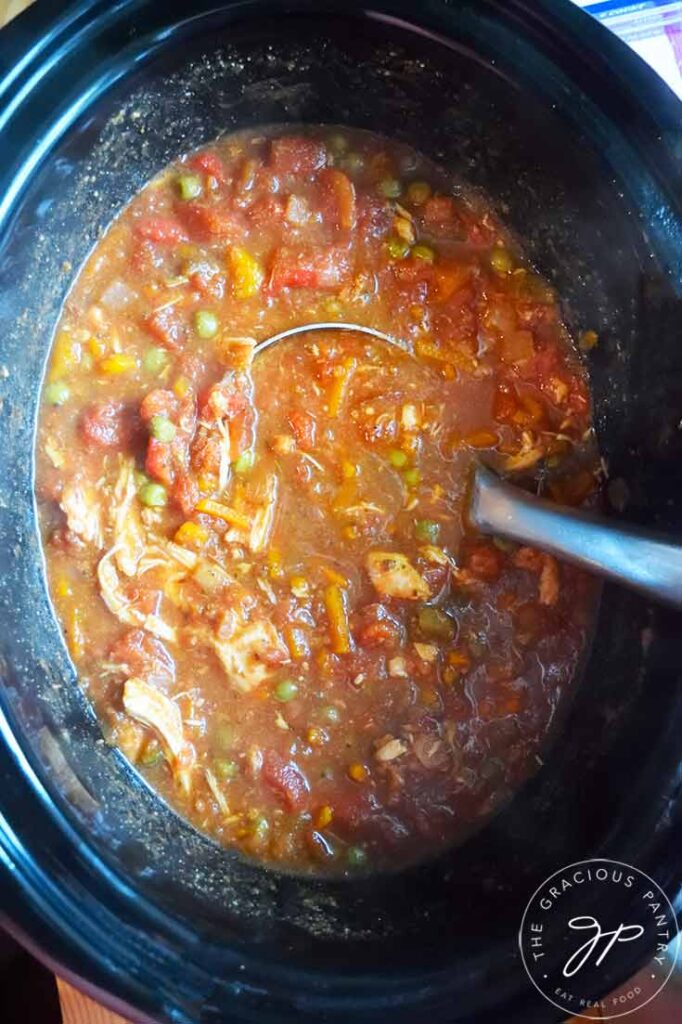 Crockpot Italian Chicken in a black slow cooker crock. A ladle rest inside the crock.