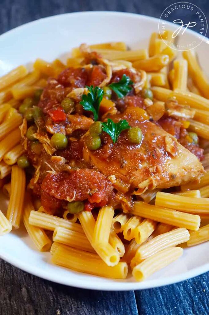 A side view of Crockpot Italian Chicken served over penne pasta in a white bowl.