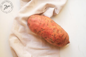 A whole sweet potato rests on a counter, next to a towel.