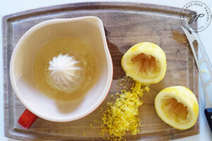 A zested and juice lemon on a cutting board next to a manual lemon juicer.