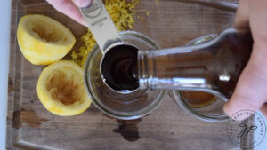 Pouring honey into a measuring spoon over two empty glasses.